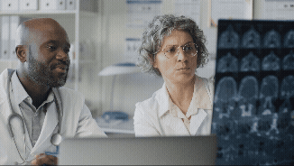 Vídeo curto decorativo animado, sem som e repetitivo, de um médico preto e uma professora branca conversando, para entender o exame de raio-X de um aluno internado no hospital.