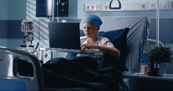 Vídeo curto decorativo animado, sem som e repetitivo, de um adolescente branco careca, que está usando um notebook para estudar sentado na cama do hospital.