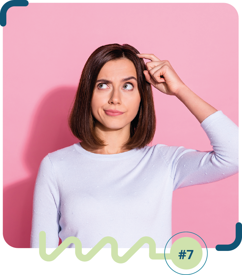 Foto colorida de uma mulher de camisa de manga longa branca, com a não esquerda na cabeça e expressão de dúvida. O fundo da imagem é rosa.