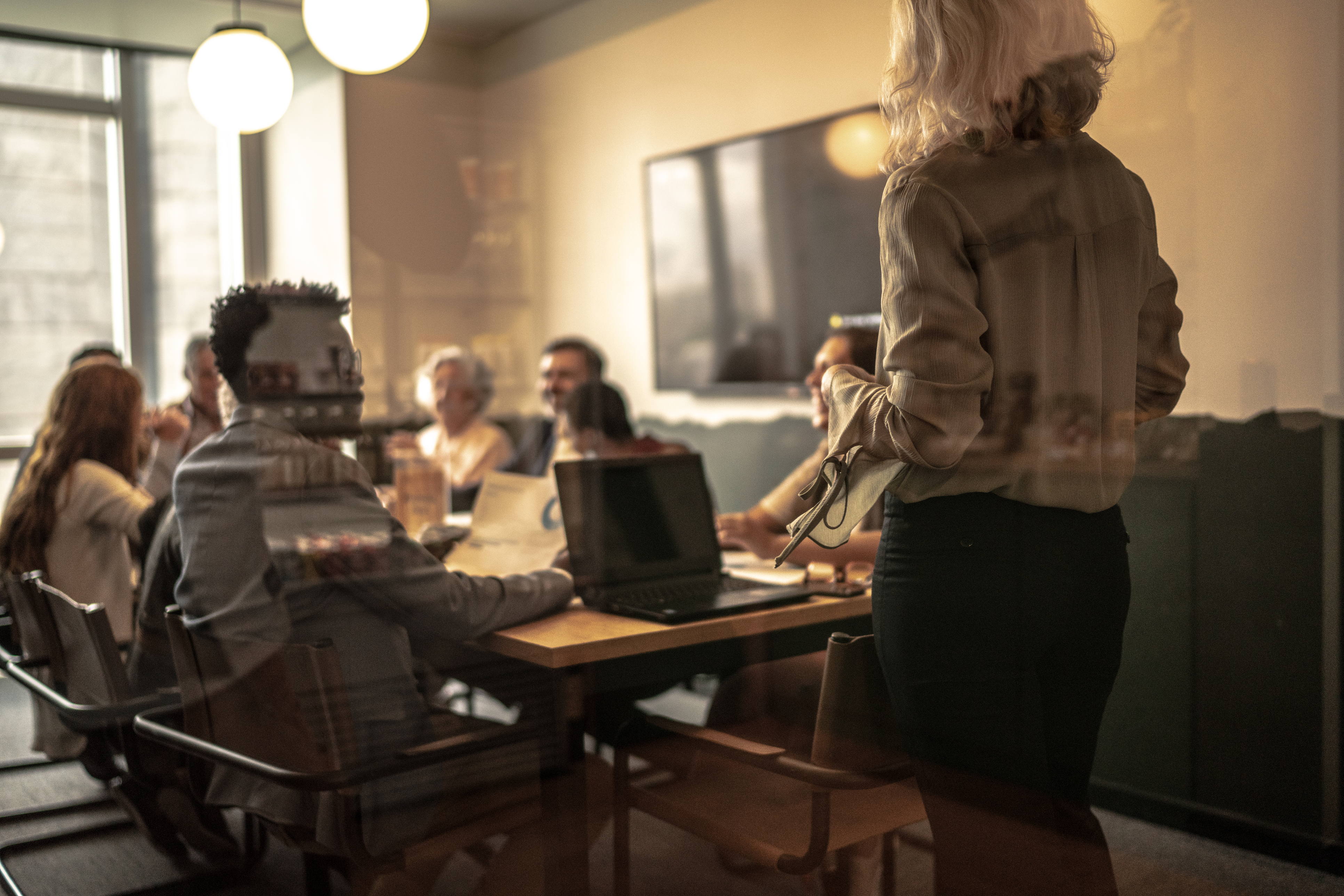 Descrição da imagem: a imagem mostra pessoas em torno de uma mesa participando de uma reunião de trabalho.
